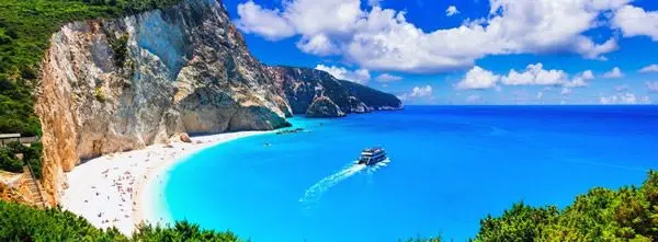 une plage splendide en Grèce. on voit un bateau s'éloigner vers le large
